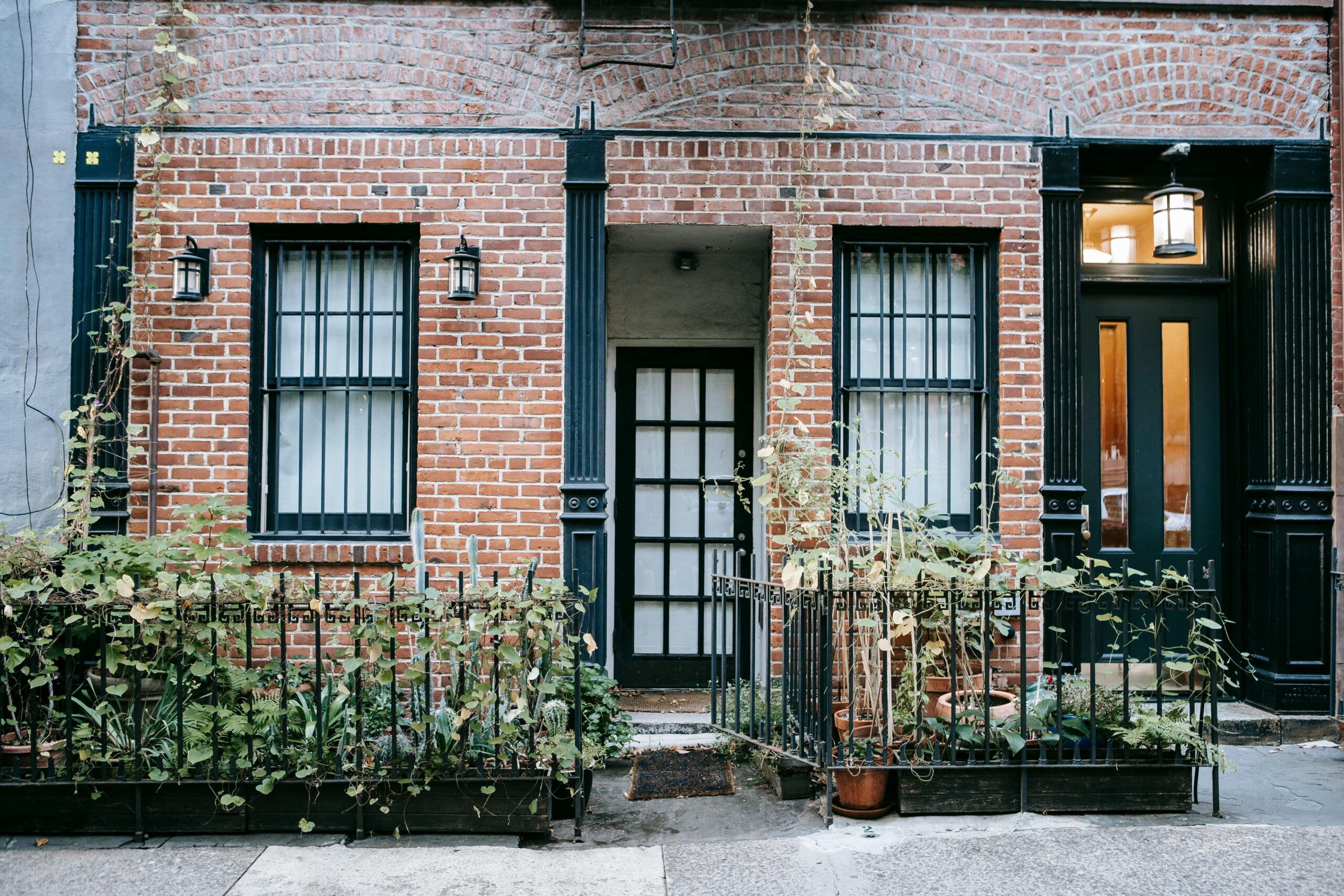 A charming brick townhouse facade with potted plants and a classic black door.